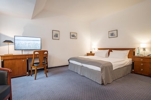 A hotel room with a bed, a desk, a chair, a television, and framed pictures on the wall. - Carstens Landhaus (Timmendorfer Strand)