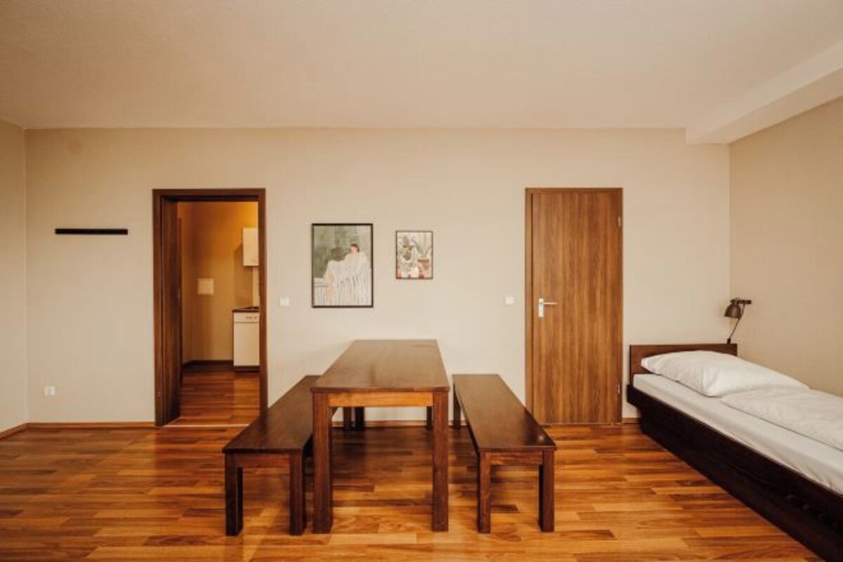 Une pièce avec un plancher en bois, un lit, une table avec des bancs et deux portes.