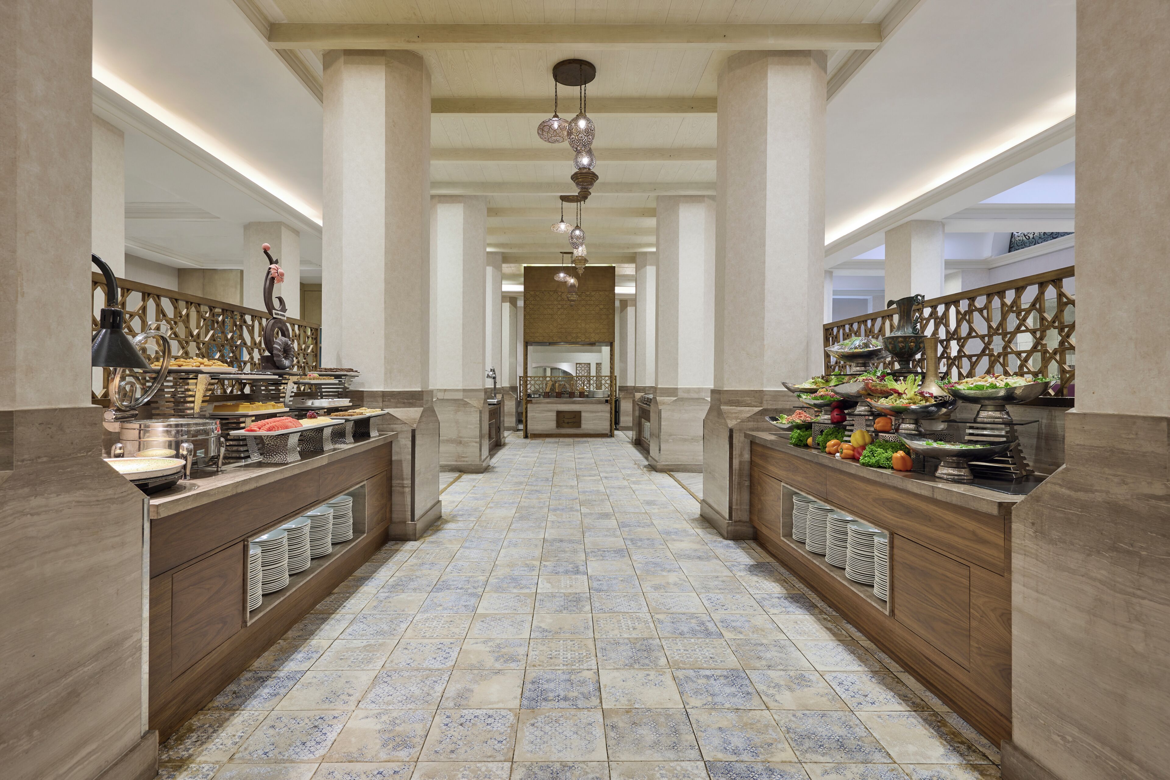 A hotel lobby with a central corridor flanked by buffet counters, a chandelier, and a patterned floor.