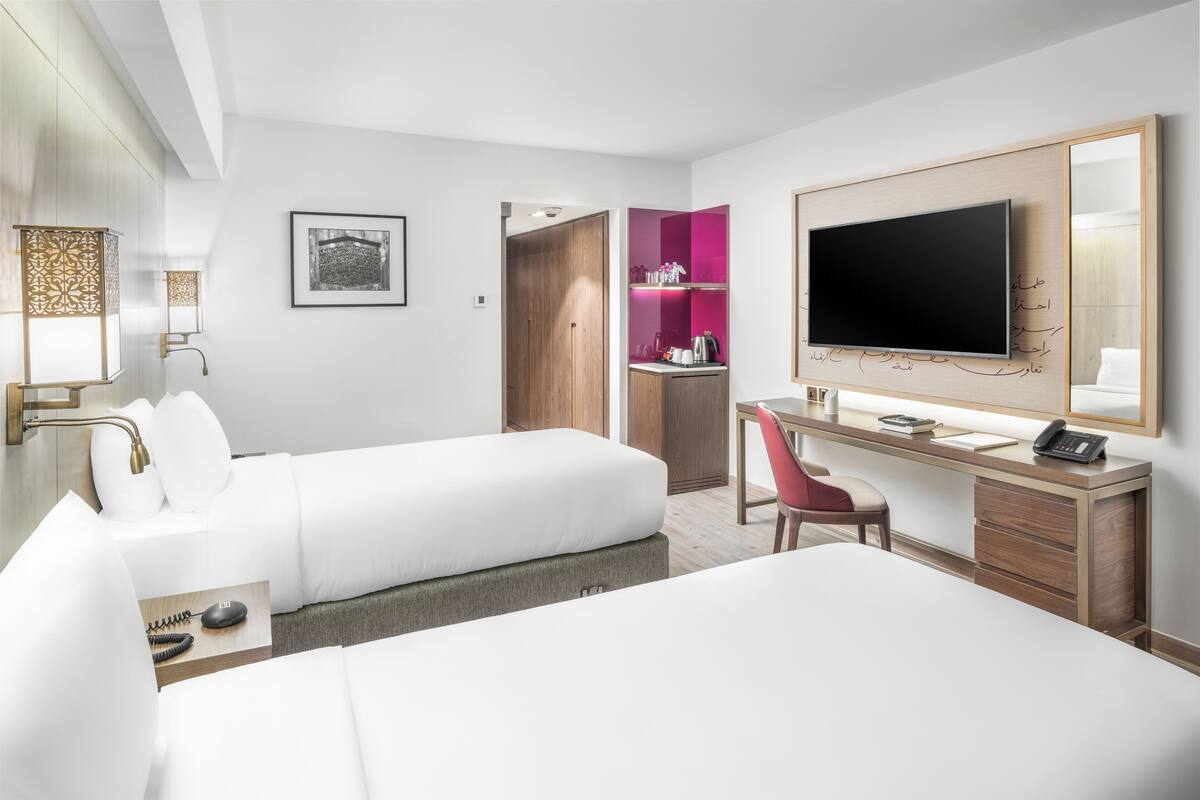 Hotelkamer met twee bedden, een bureau met stoel, een televisie, een kledingkast en een badkamer met douche en toilet.