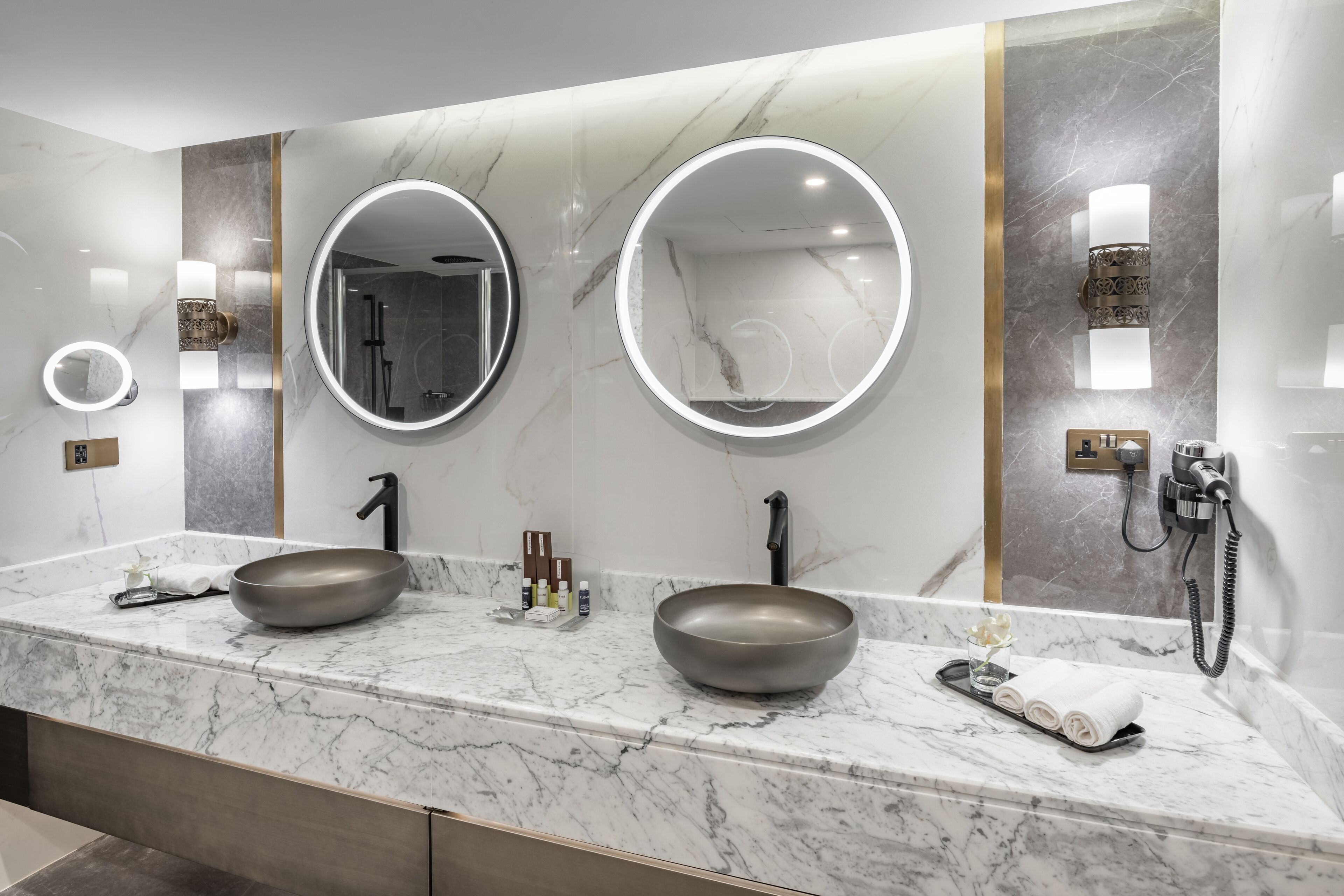 A modern bathroom with two sinks, marble countertops, and wall-mounted mirrors.