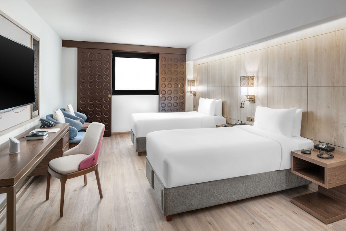 Een hotelkamer met twee bedden, een bureau, een stoel, een televisie en een raam met uitzicht.