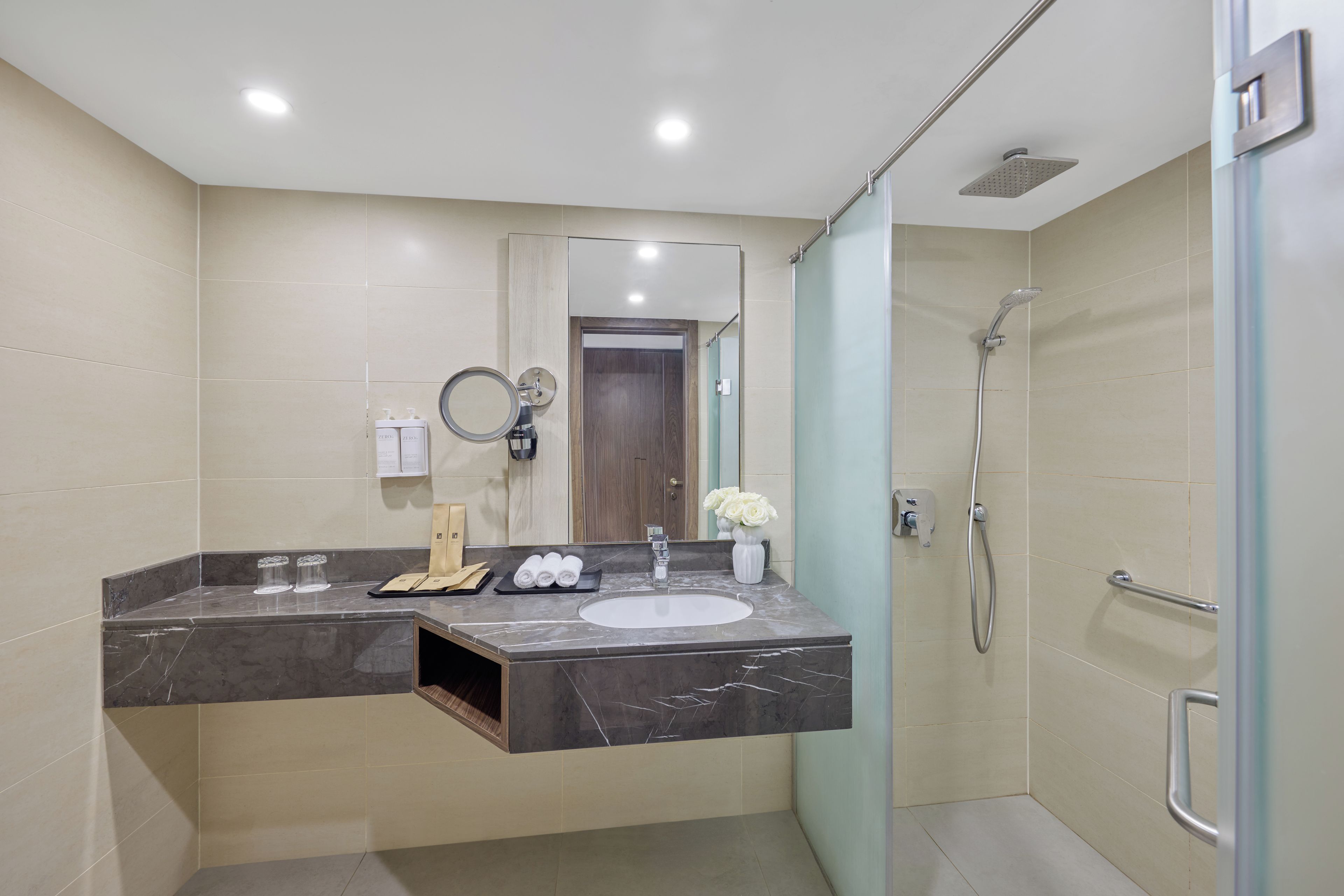 A modern bathroom with a marble sink, a handheld showerhead, and a mirror with a round frame.