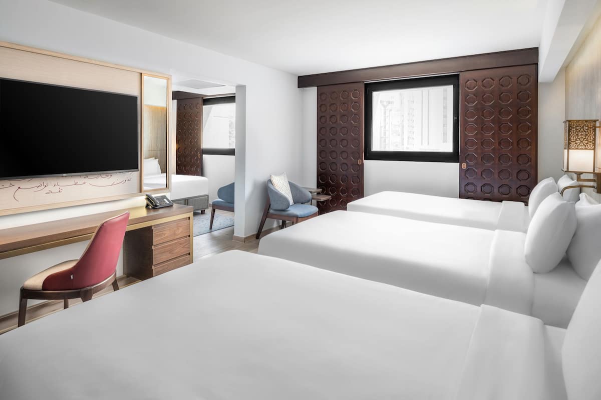 Hotelkamer met een groot bed, een bureau met stoel, een televisie en een raam met uitzicht op gebouwen.