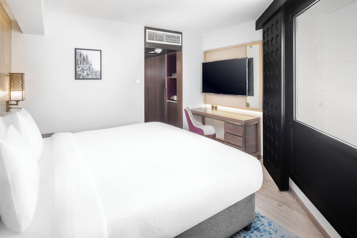 Hotelkamer met een groot bed, een bureau met stoel, een flatscreen televisie, een garderobe en een wandairconditioning.