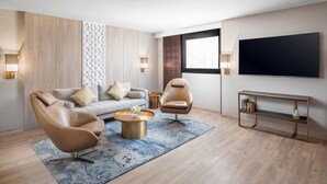 Un salon moderne comprenant un canapé, deux fauteuils, une table basse, un téléviseur et une bibliothèque.