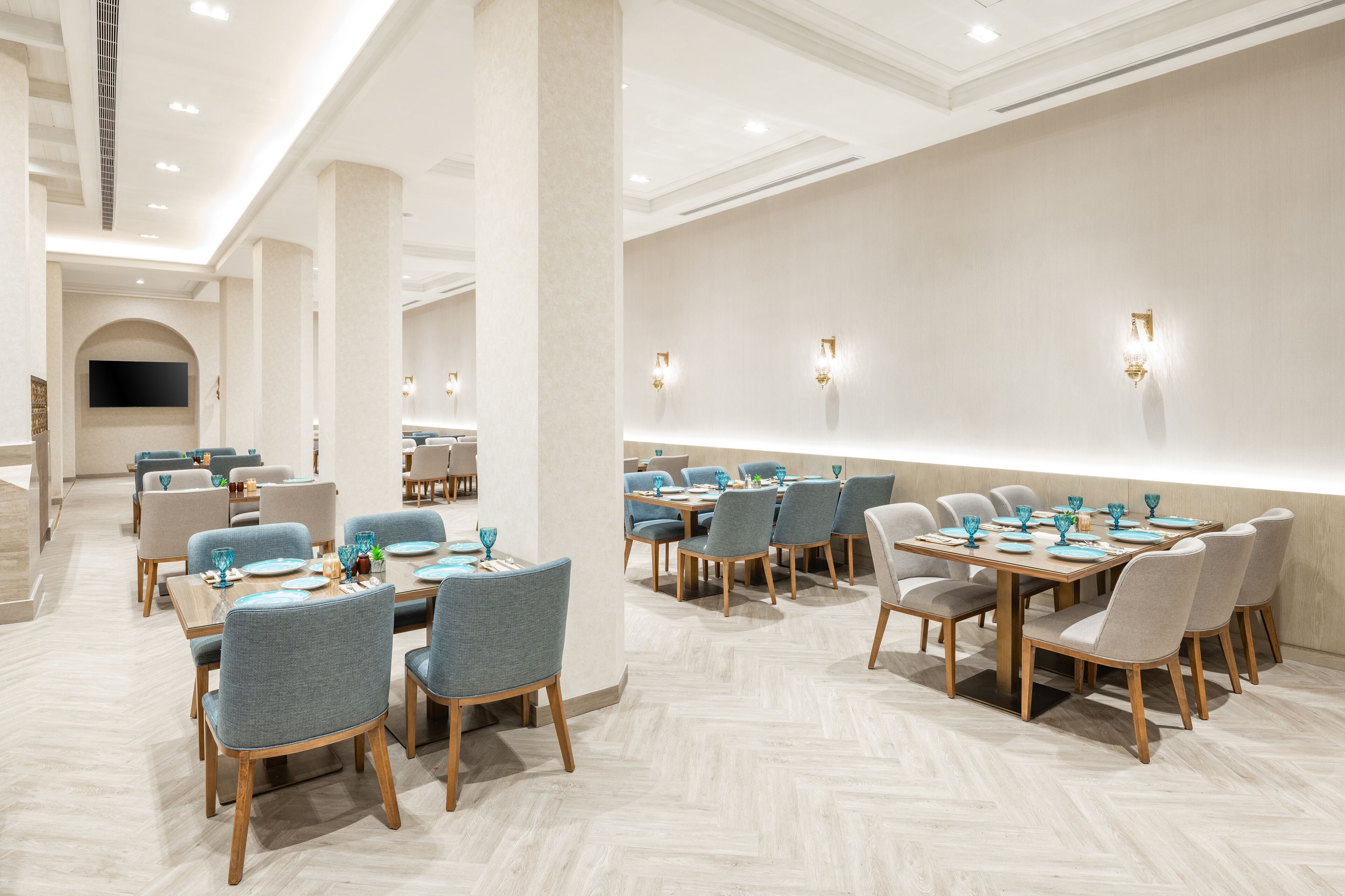 A modern dining area with multiple tables and chairs, a flat-screen TV mounted on the wall, and recessed lighting.
