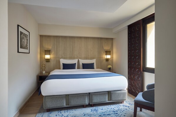 Une chambre d’hôtel moderne avec un grand lit, deux lampes de chevet, une tête de lit en bois et une vue sur l’extérieur par une porte.