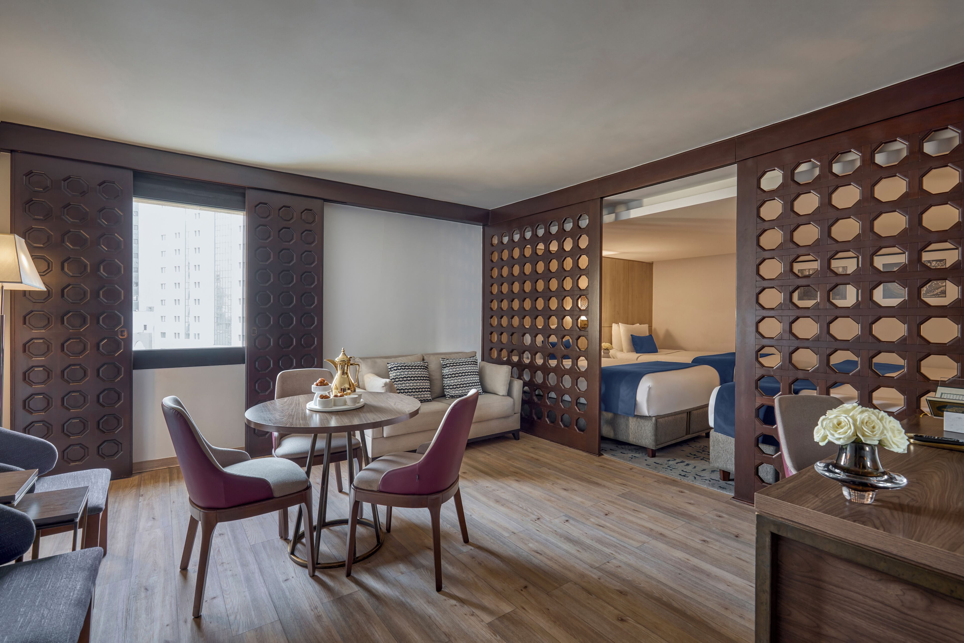 Een hotelkamer met een eethoek, een bank, een bed en een decoratief scheidingswand met honingraatmotieven.