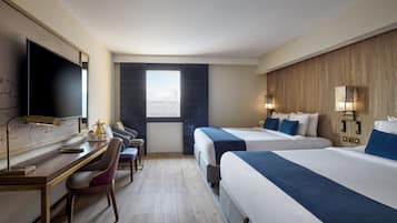 Habitación de hotel con dos camas, un escritorio, una silla, un televisor y una ventana con vistas a edificios.