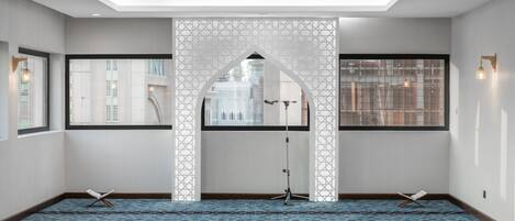 Una sala de oración con alfombra estampada, un arco decorativo blanco y un micrófono montado sobre un trípode.