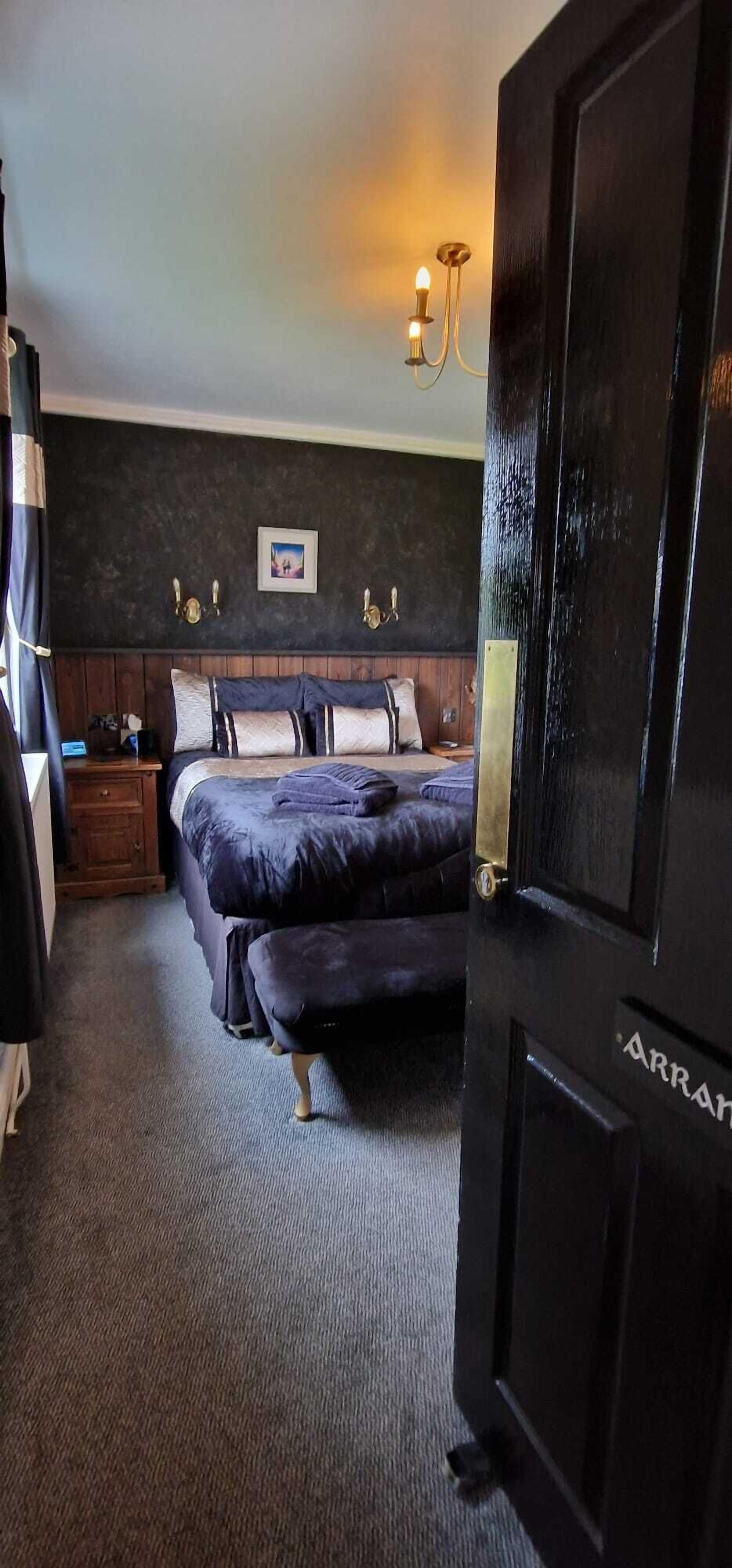 Une chambre à coucher avec une tête de lit en bois foncé, un lit avec une literie aux couleurs sombres, une table de chevet avec une lampe et un tableau accroché au mur.