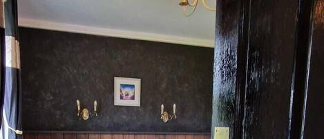 Une chambre à coucher avec une tête de lit en bois foncé, un lit avec une literie aux couleurs sombres, une table de chevet avec une lampe et un tableau accroché au mur.