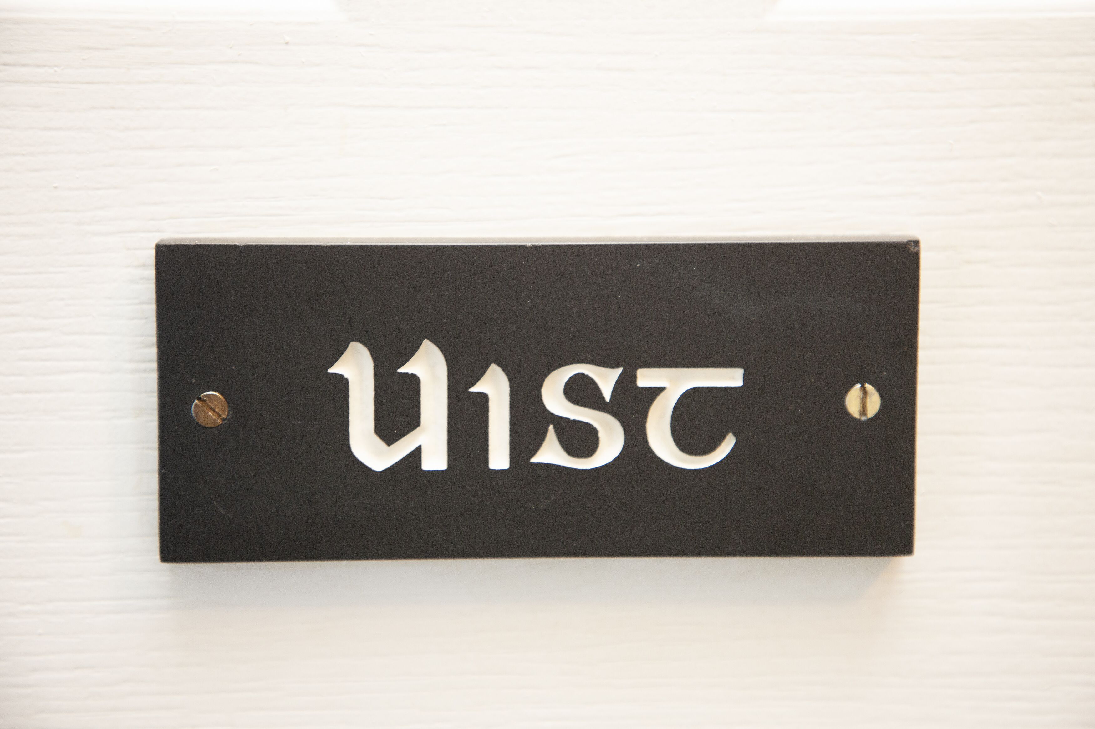 A black sign with white letters spelling "U1ST" mounted on a white wall.