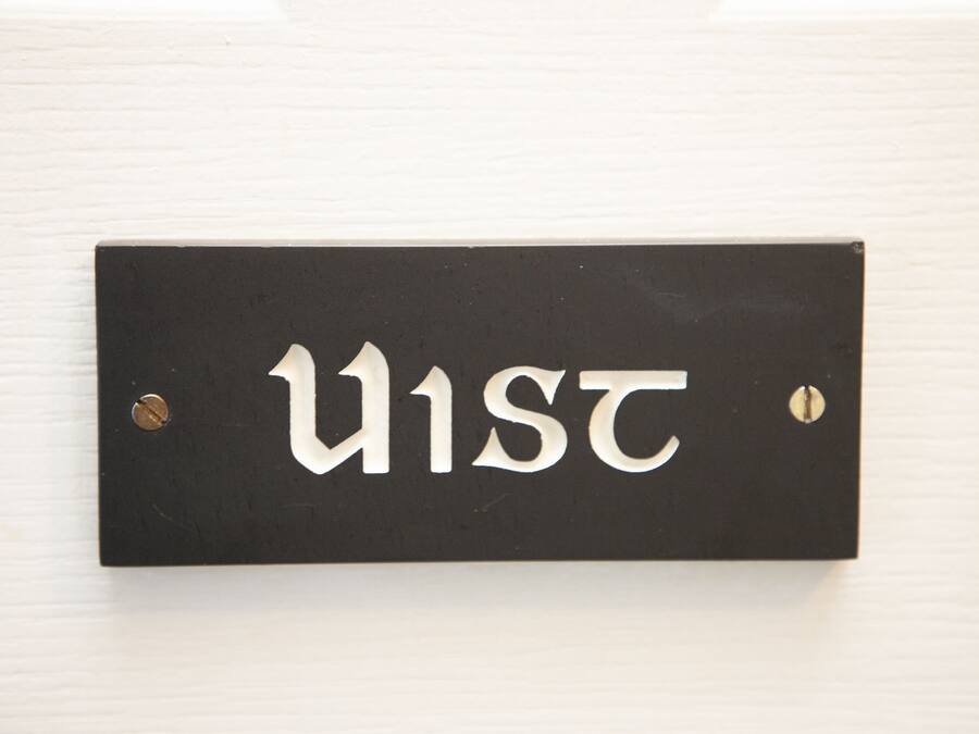A black sign with white letters spelling "U1ST" mounted on a white wall.