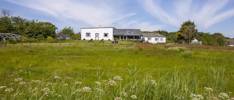 Ein weißes Bauernhaus mit großer Veranda und einem Stall in einem grasbewachsen Feld.