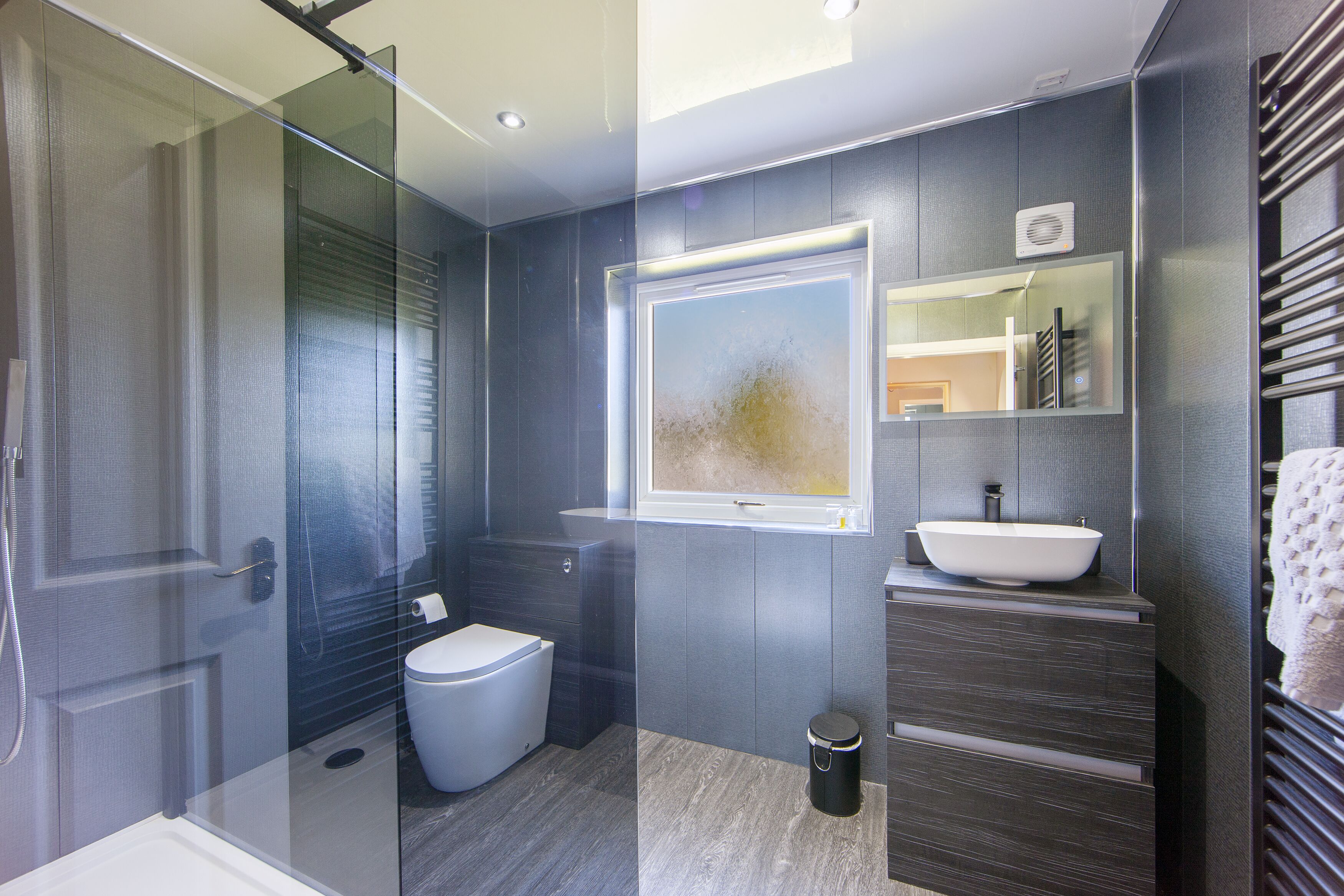 A modern bathroom with a glass shower enclosure, a white toilet, a large mirror, and a vessel sink.