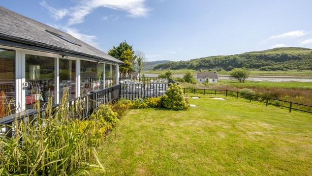 A building with a glass facade, a grassy lawn, and a view of a hilly landscape. - The Galley of Lorne Inn (Lochgilphead)