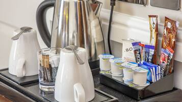 Una estación de café con una cafetera, dos tazas de café y una bandeja con cápsulas de café y sobres de crema.