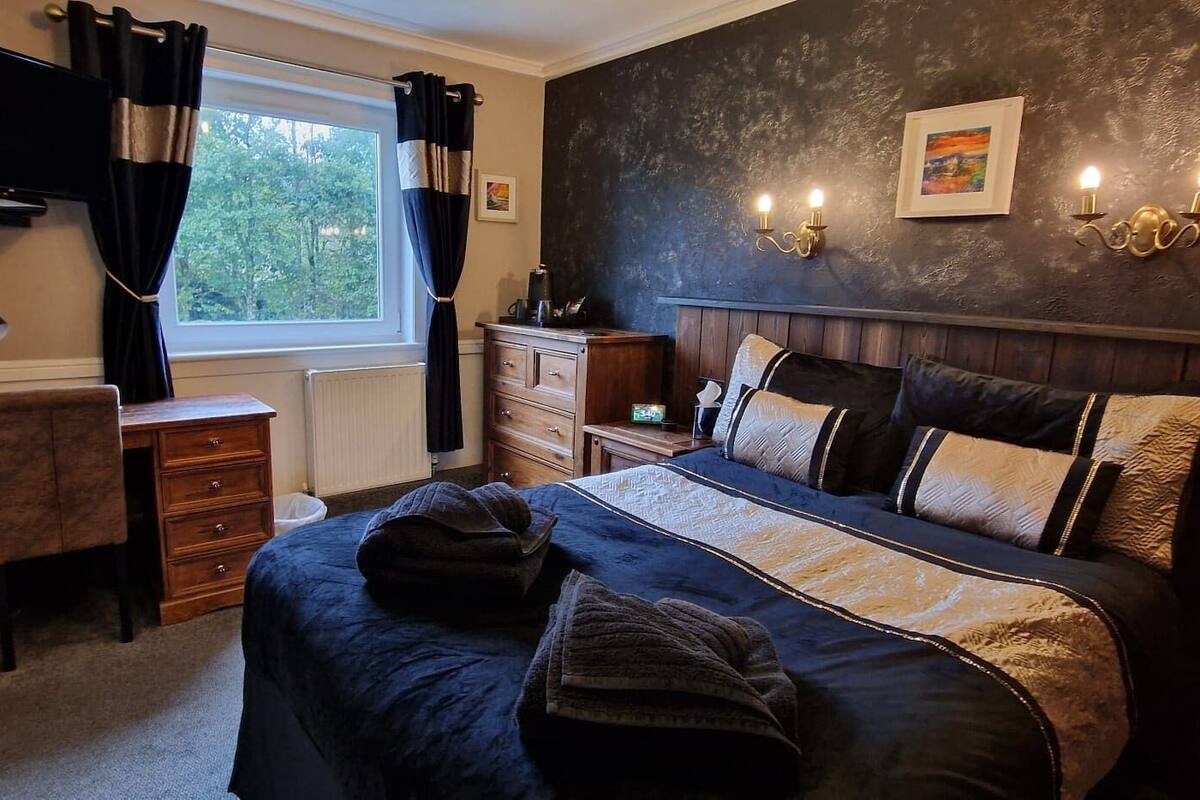 Un dormitorio con cama, cómoda, escritorio y ventana con cortinas.