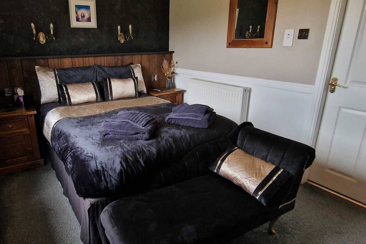 Un dormitorio con cama, dos mesitas de noche, una silla, un radiador y una puerta.