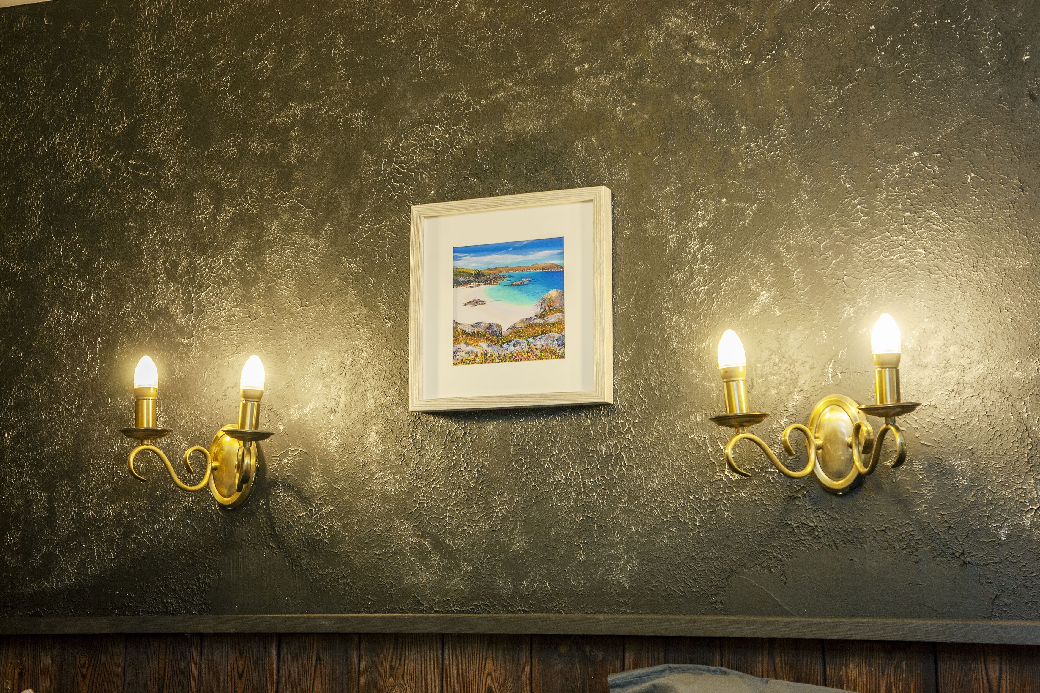 Una pared con textura, dos lámparas fijadas a la pared y un cuadro con una imagen de playa.