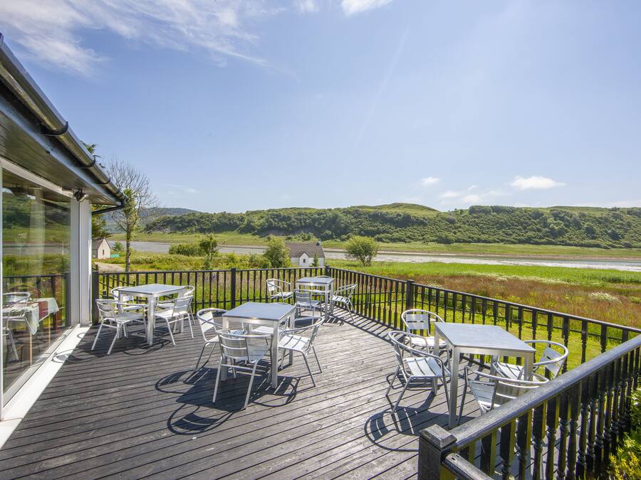 A deck with outdoor seating and a view of a river and hills.