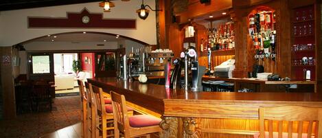 A bar area with wooden bar stools, a counter, and a variety of bottles and glasses.