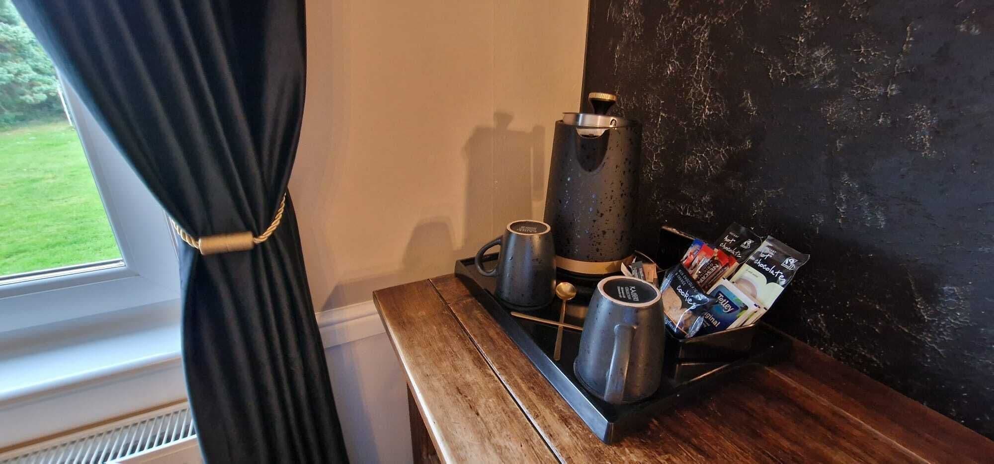 Een koffiehoek met een koffiezetapparaat, twee mokken en een dienblad met koffiezakjes.