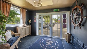 A hotel lobby with a wicker sofa, a ship's wheel, and a fire exit sign. - The Galley of Lorne Inn (Lochgilphead)