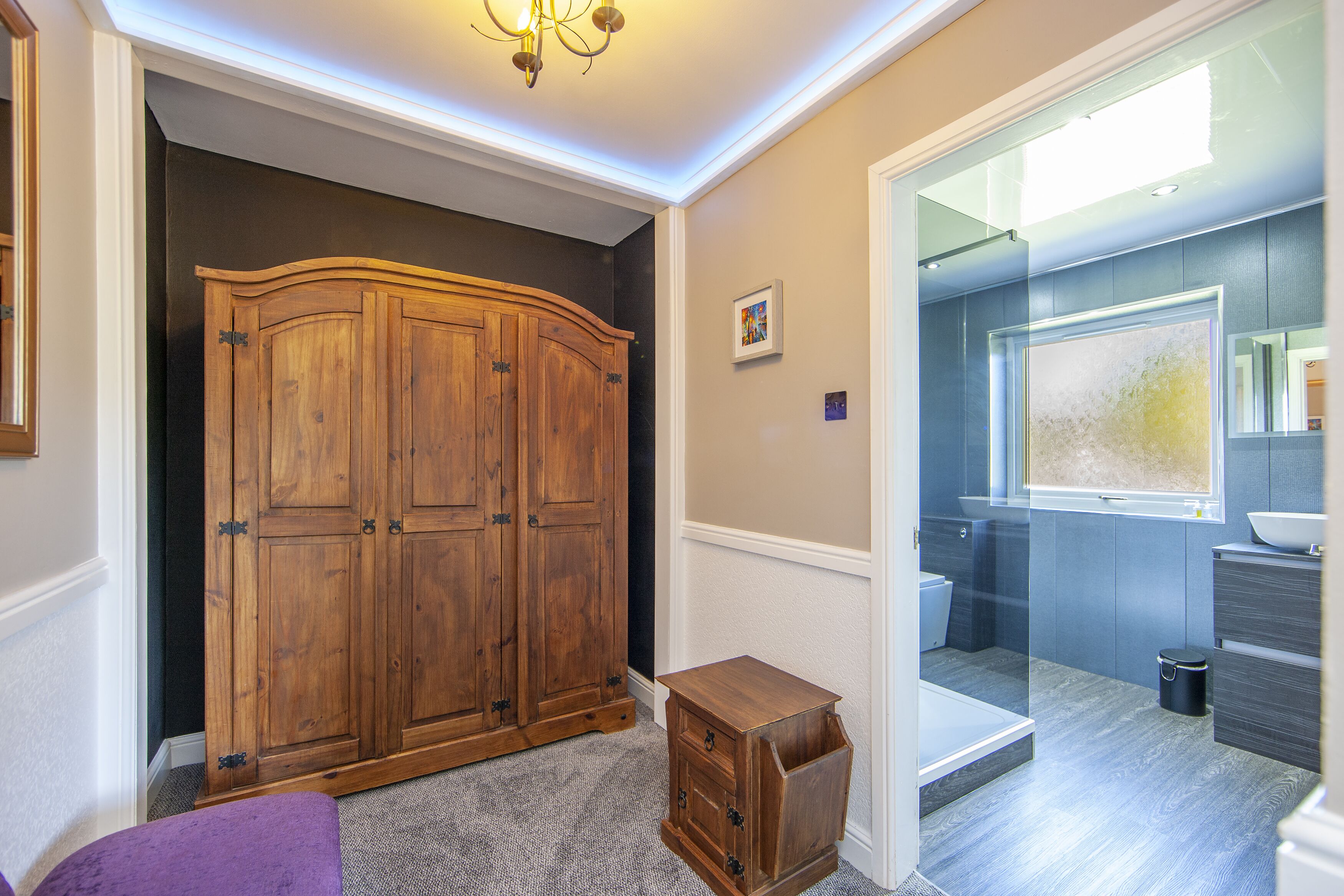 A bathroom with a wooden cabinet, a small wooden stool, and a glass shower enclosure.