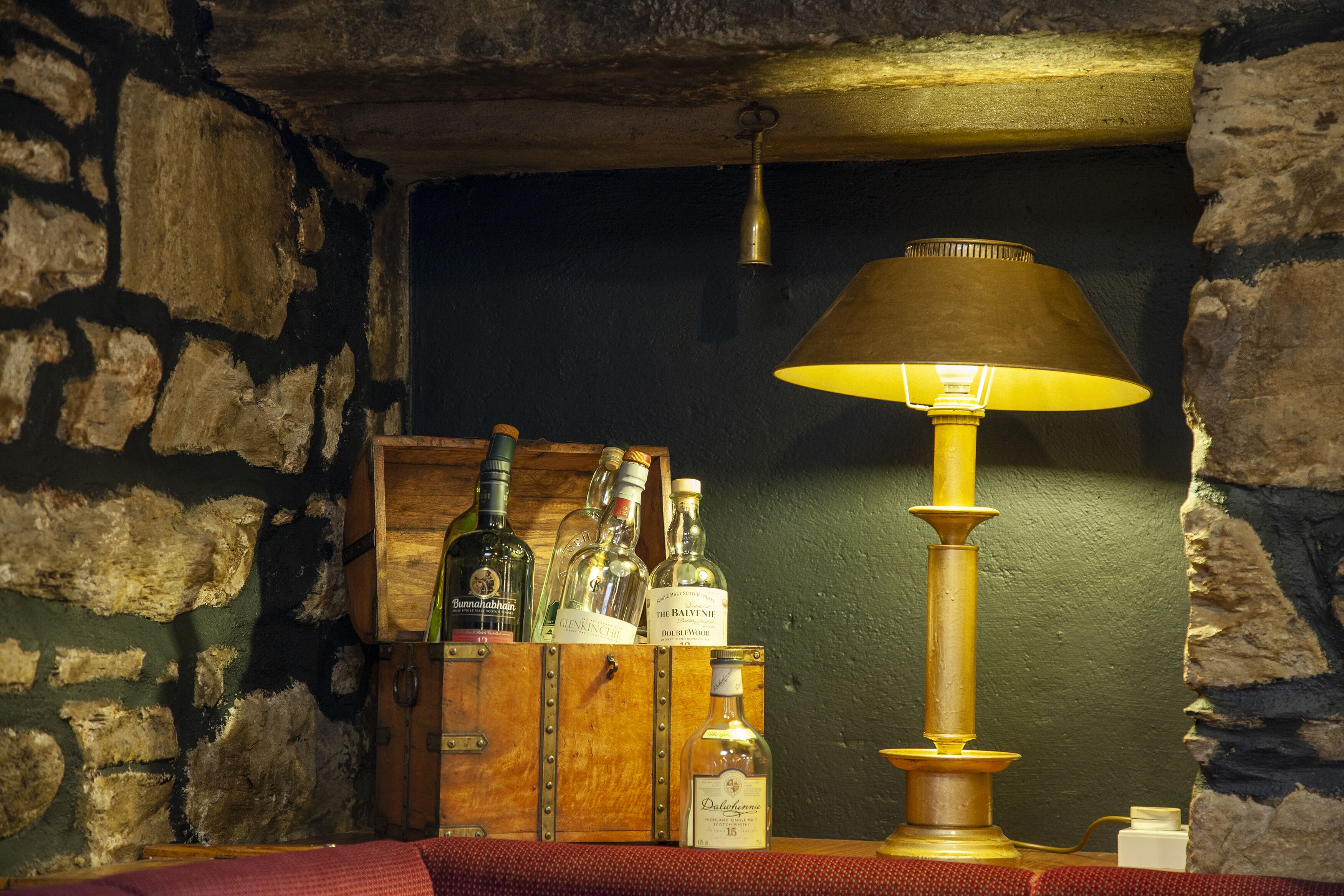 A wooden cabinet with bottles of alcohol, a brass lamp, and a stone wall.