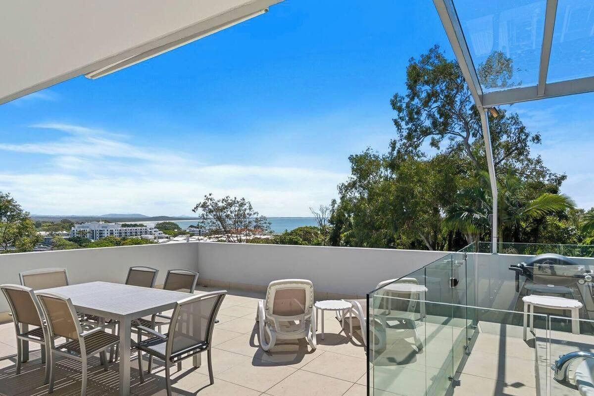 A balcony with a glass enclosure, outdoor furniture, and a view of the sea and buildings.