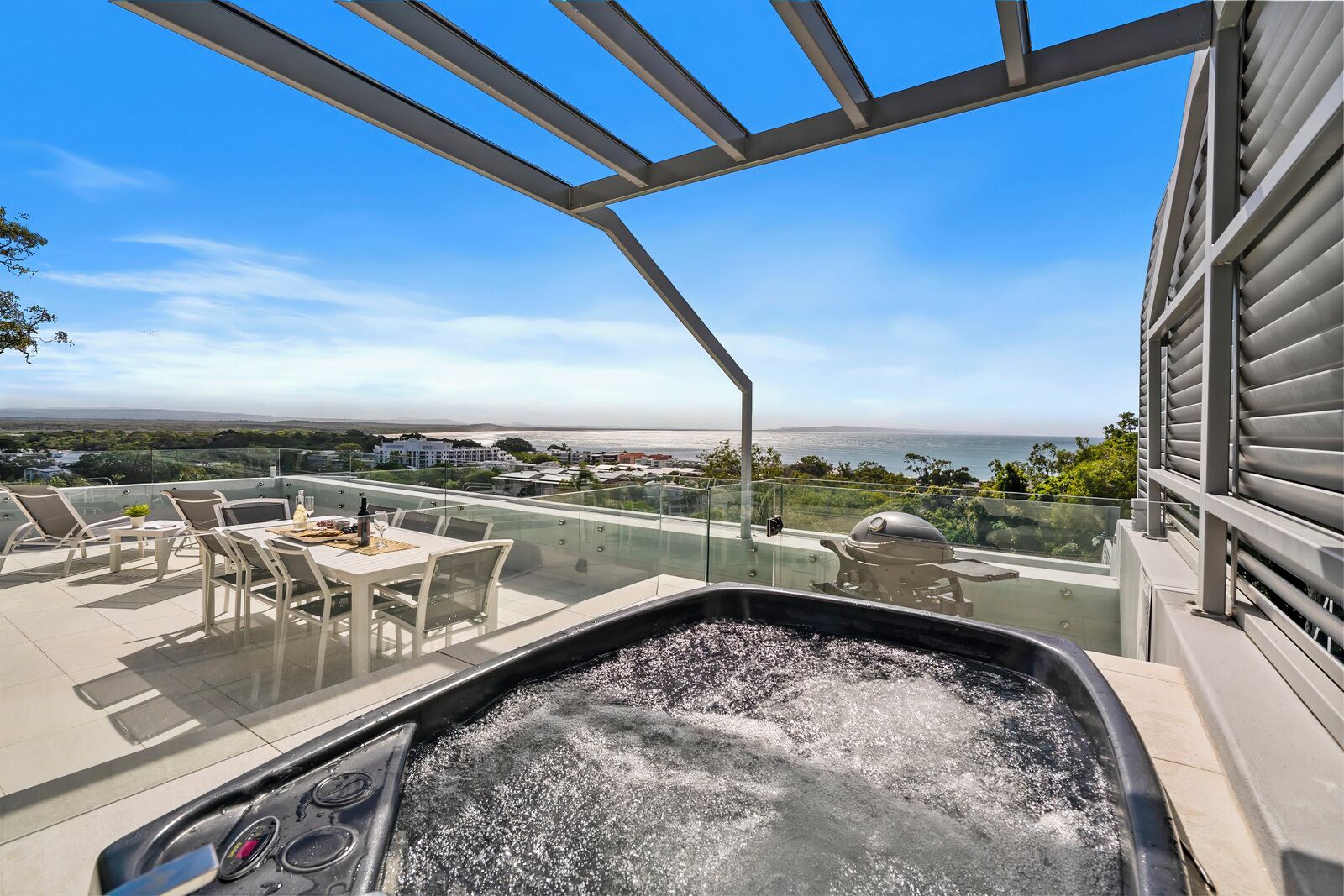 Terraza en la azotea con jacuzzi, barandilla de cristal, mobiliario exterior y vista al océano.