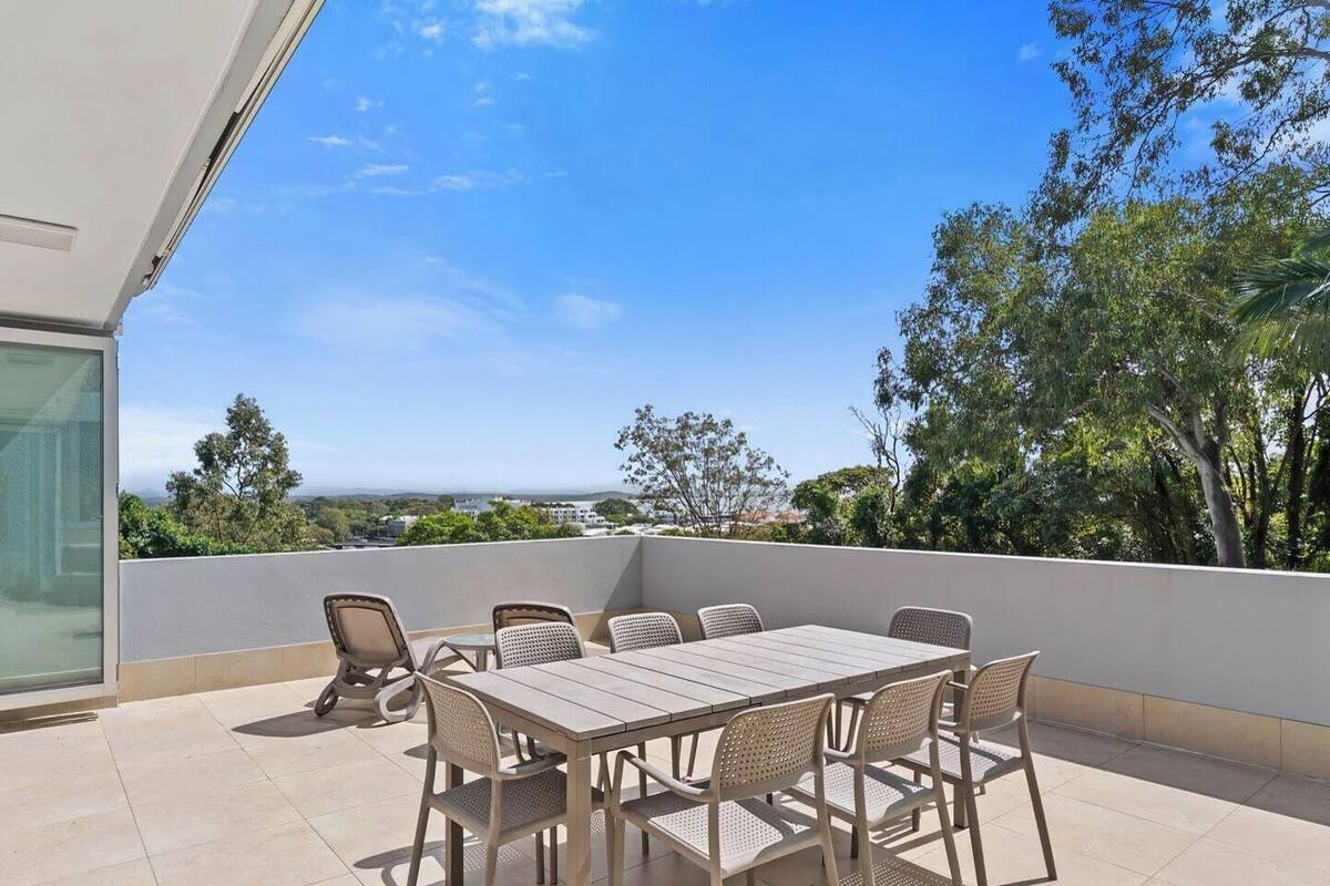 A balcony with a table and chairs, a glass door, and a view of the landscape.
