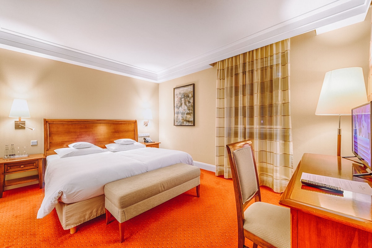 A hotel room with a large bed, a desk with a chair, a TV, and a window with curtains.