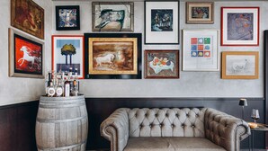 Um quarto com um sofá cinza estofado, um barril de madeira e diversas obras de arte emolduradas na parede.