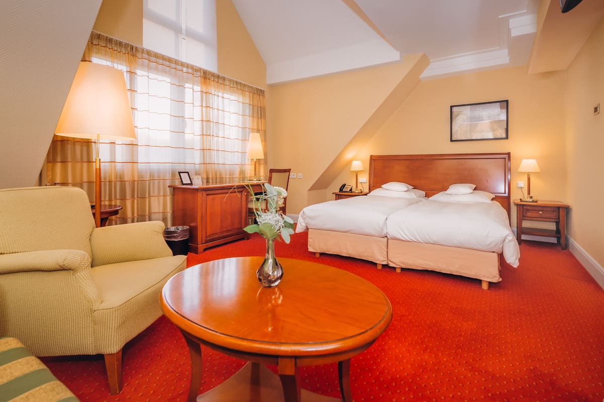 A hotel room with a bed, a chair, a table, and a vase with flowers.