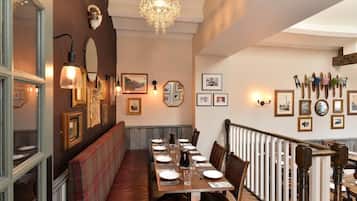 A dining area with a long table set for a meal, wooden chairs, a bench along the wall, and a chandelier.