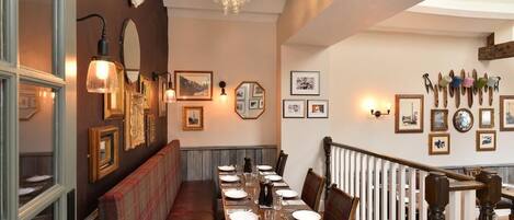 A dining area with a long table set for a meal, wooden chairs, a bench along the wall, and a chandelier.
