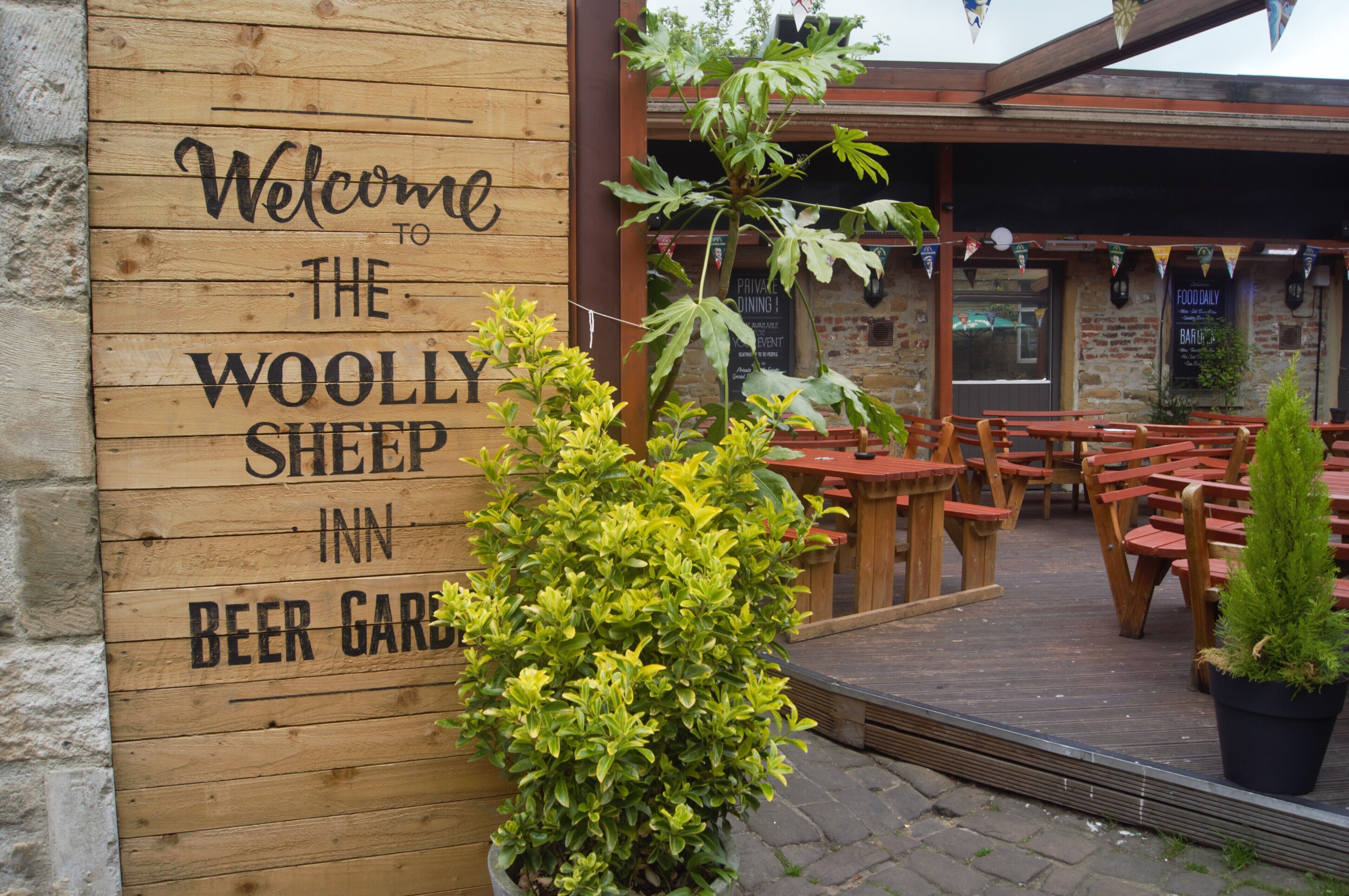 Une pancarte en bois souhaite la bienvenue aux visiteurs de l’auberge The Woolly Sheep Inn, qui dispose d’un jardin à bière avec des tables à l’extérieur.