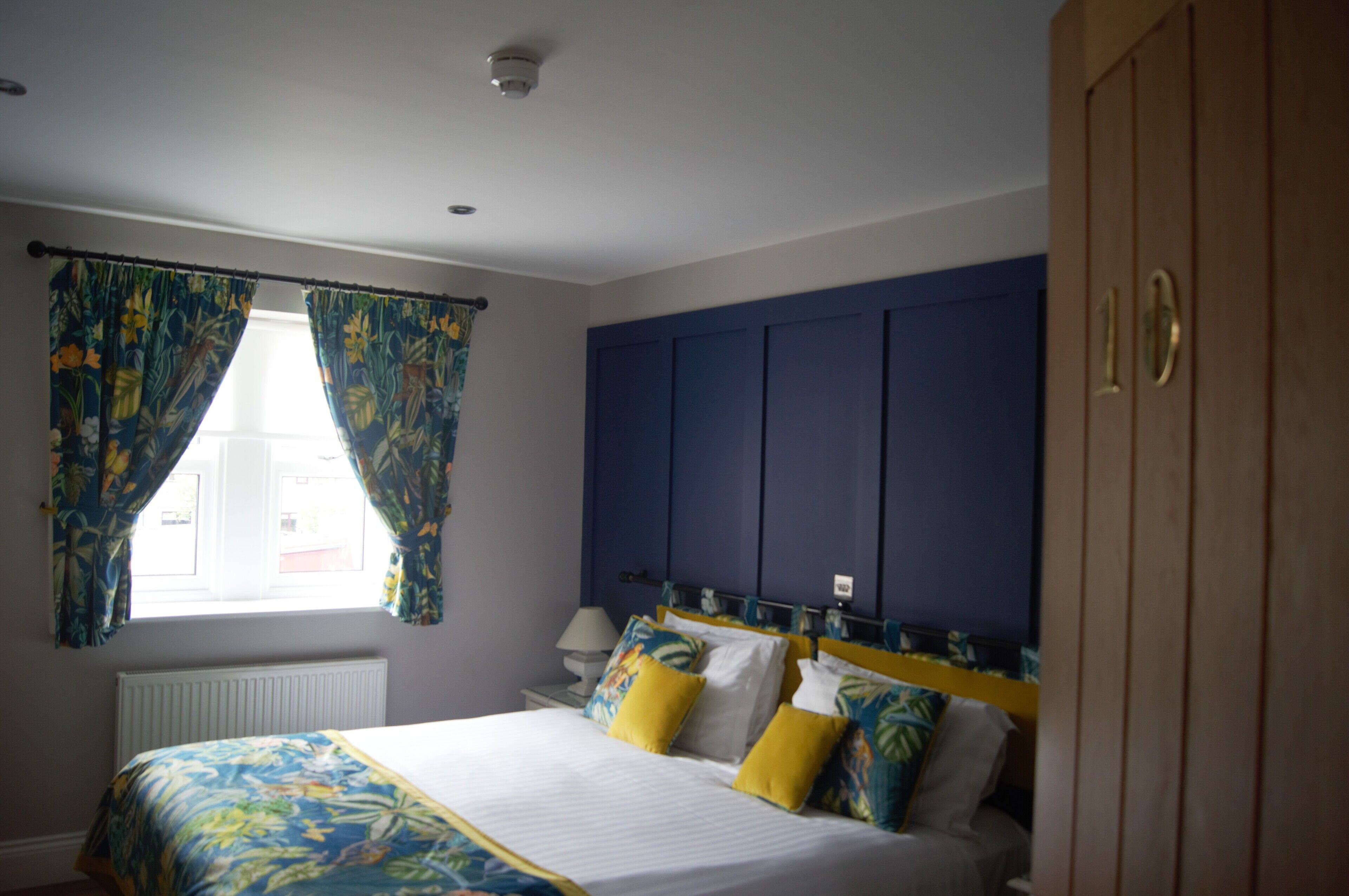 A bedroom with a bed, curtains, a nightstand, a lamp, and a wardrobe.