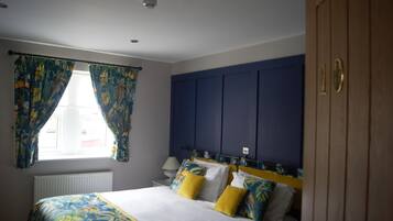 Un dormitorio con cama, cortinas, mesita de noche, lámpara y armario.