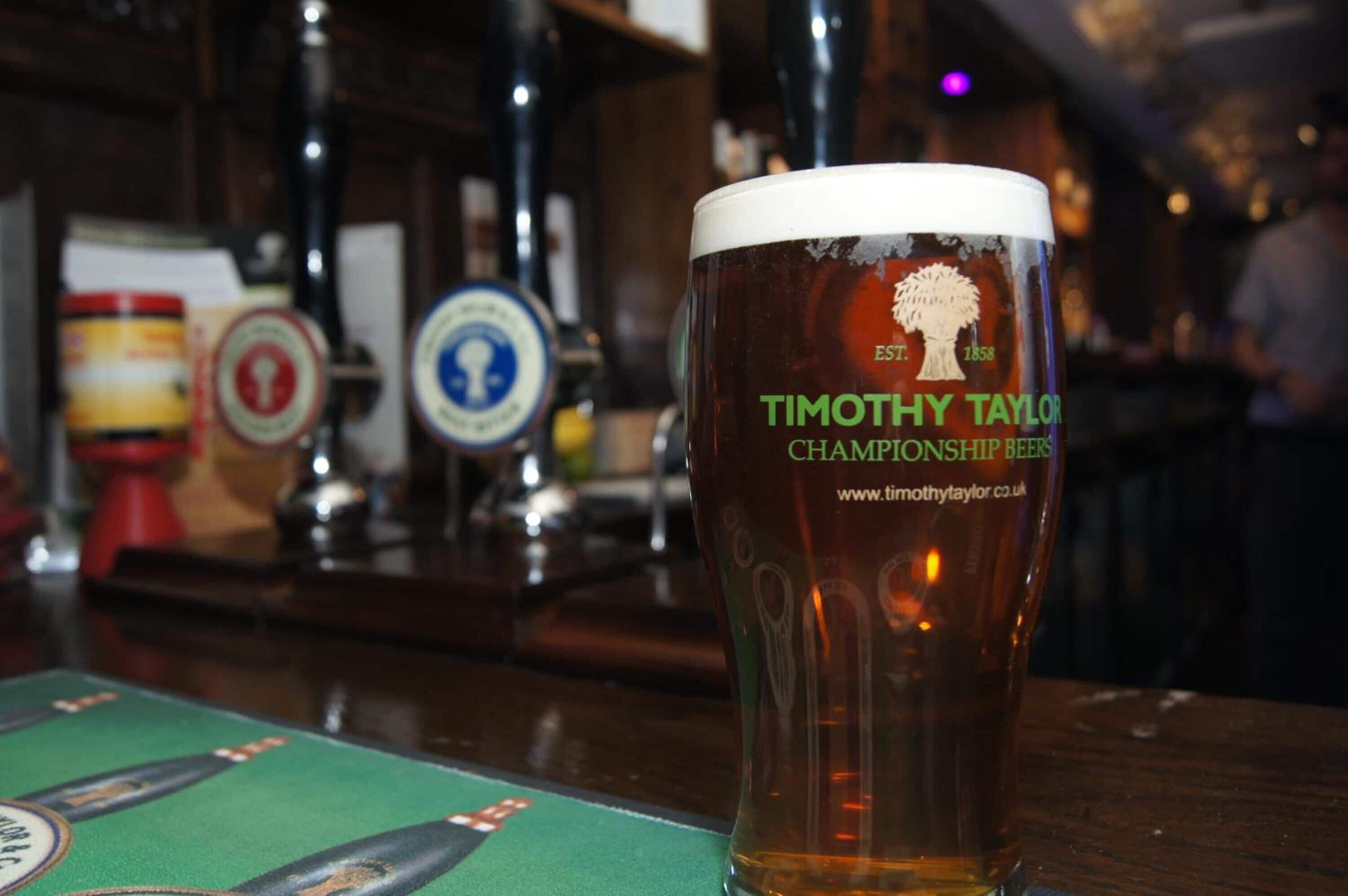 Una jarra de cerveza con la marca "Timothy Taylor Championship Beers" sobre una barra.