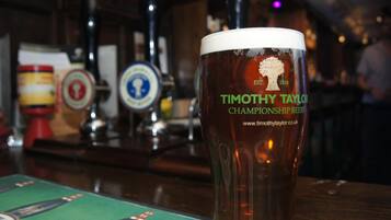A glass of beer with "Timothy Taylor Championship Beers" branding on a bar counter.