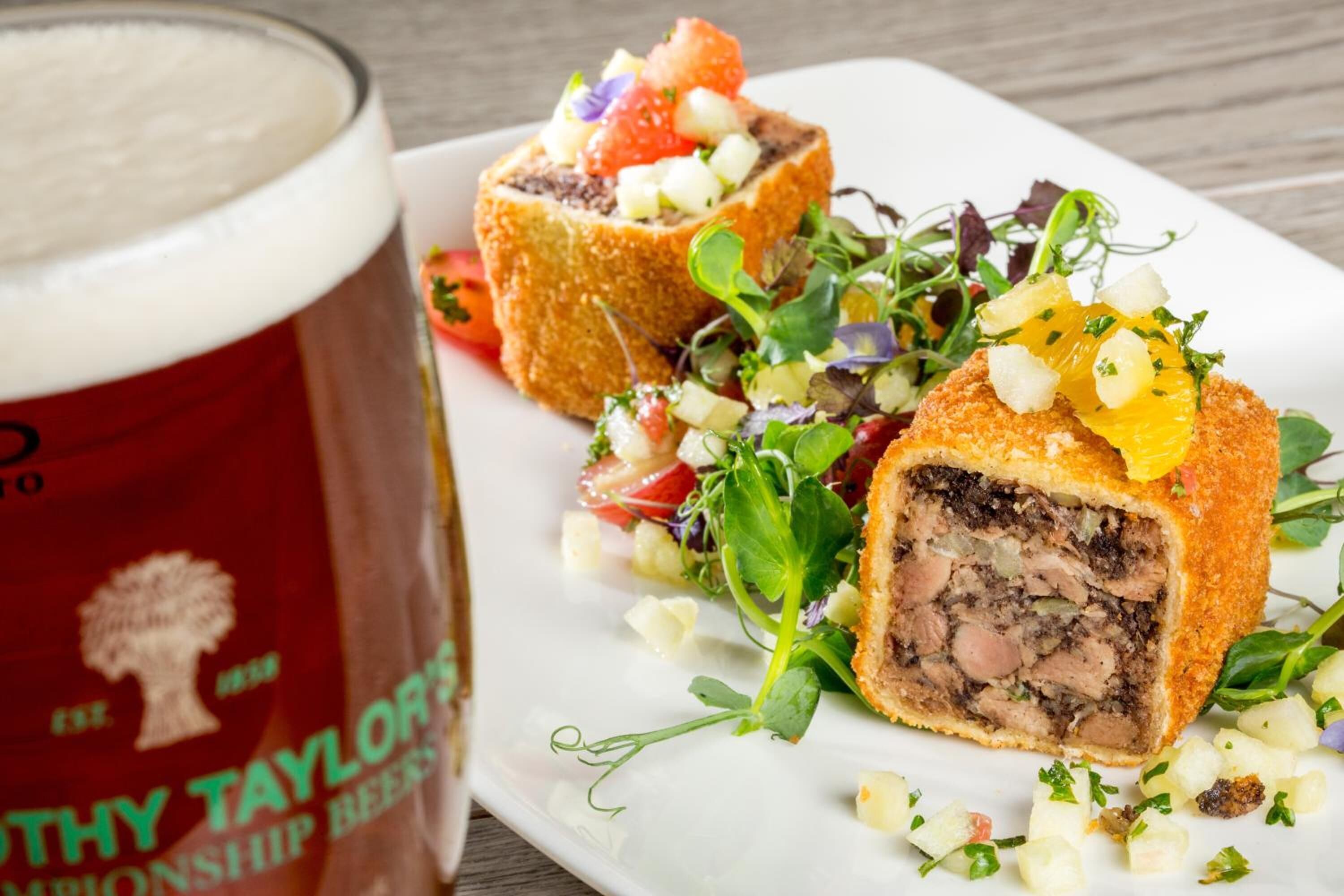 Un plato con rollitos de carne empanizados, una ensalada y una jarra de cerveza.
