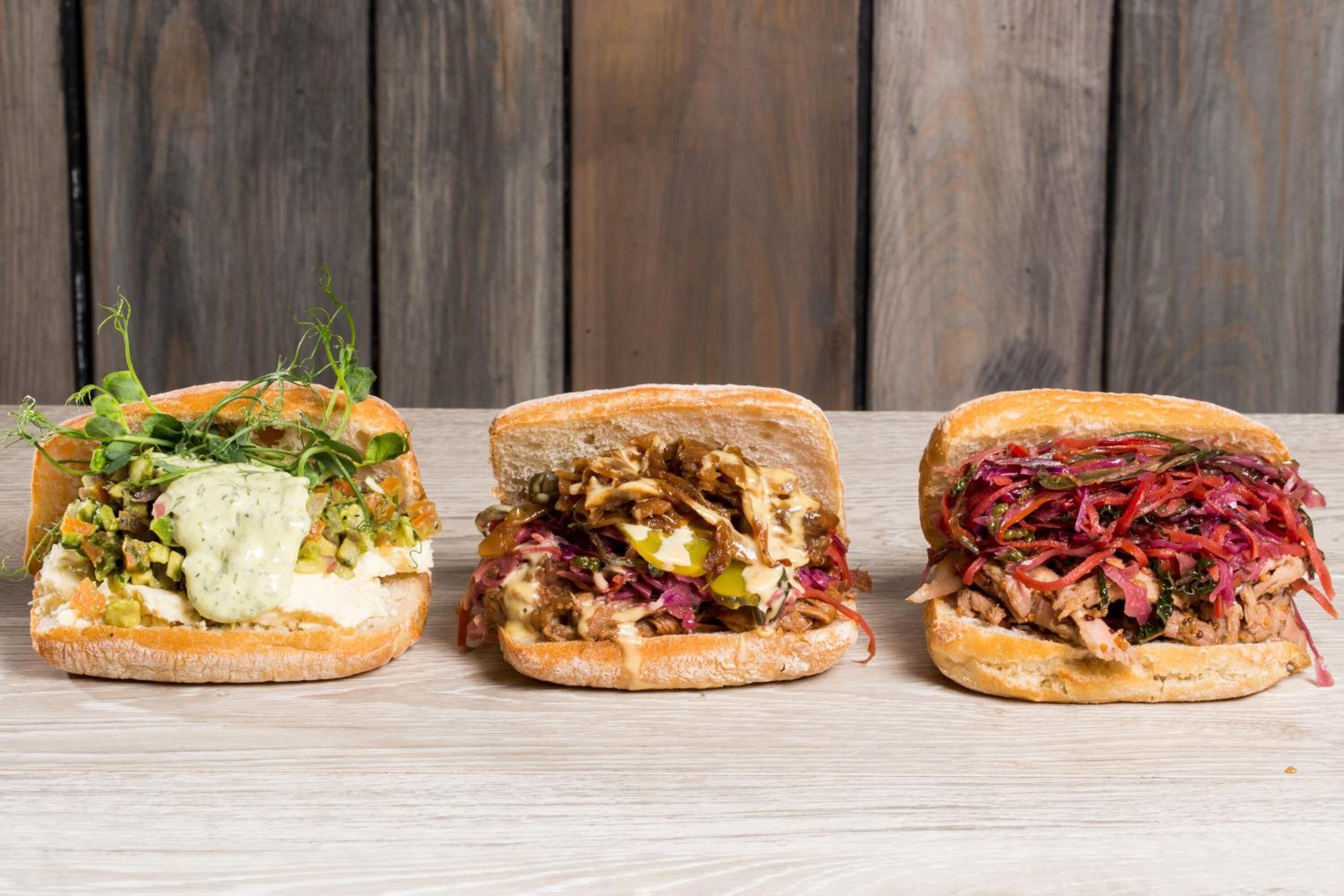 Three sandwiches on a wooden surface.
