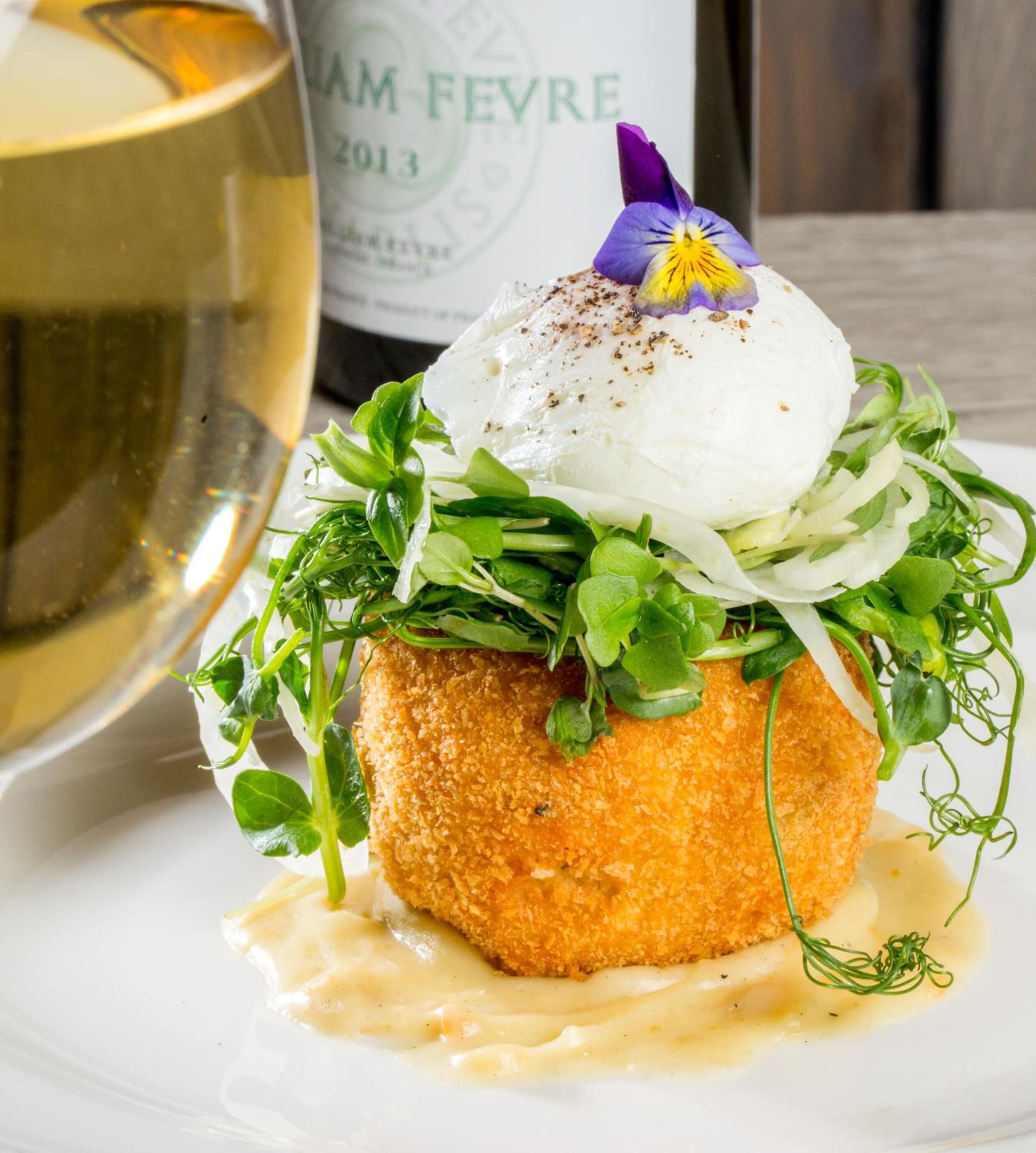 A plated dish with a poached egg, greens, and sauce, accompanied by a bottle of wine.