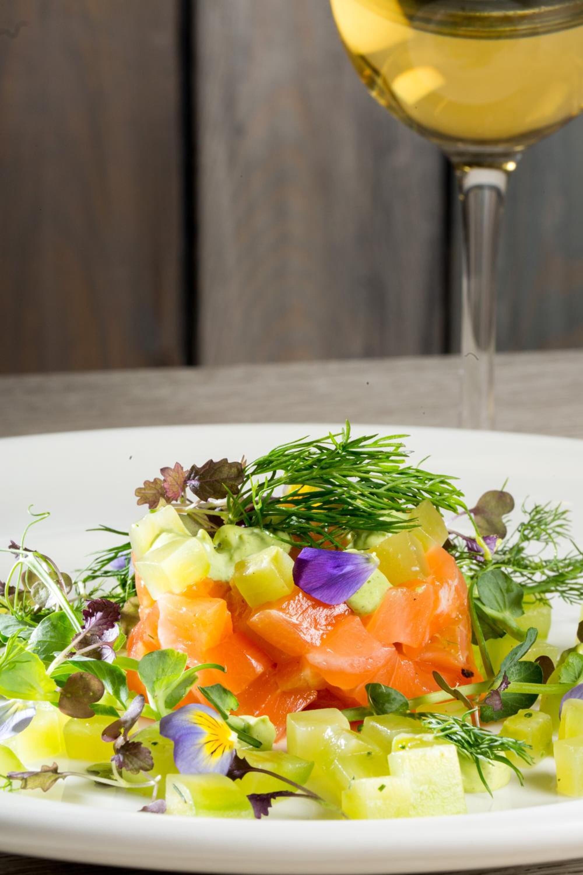 Un plato de comida con salmón, verduras y una copa de vino blanco.