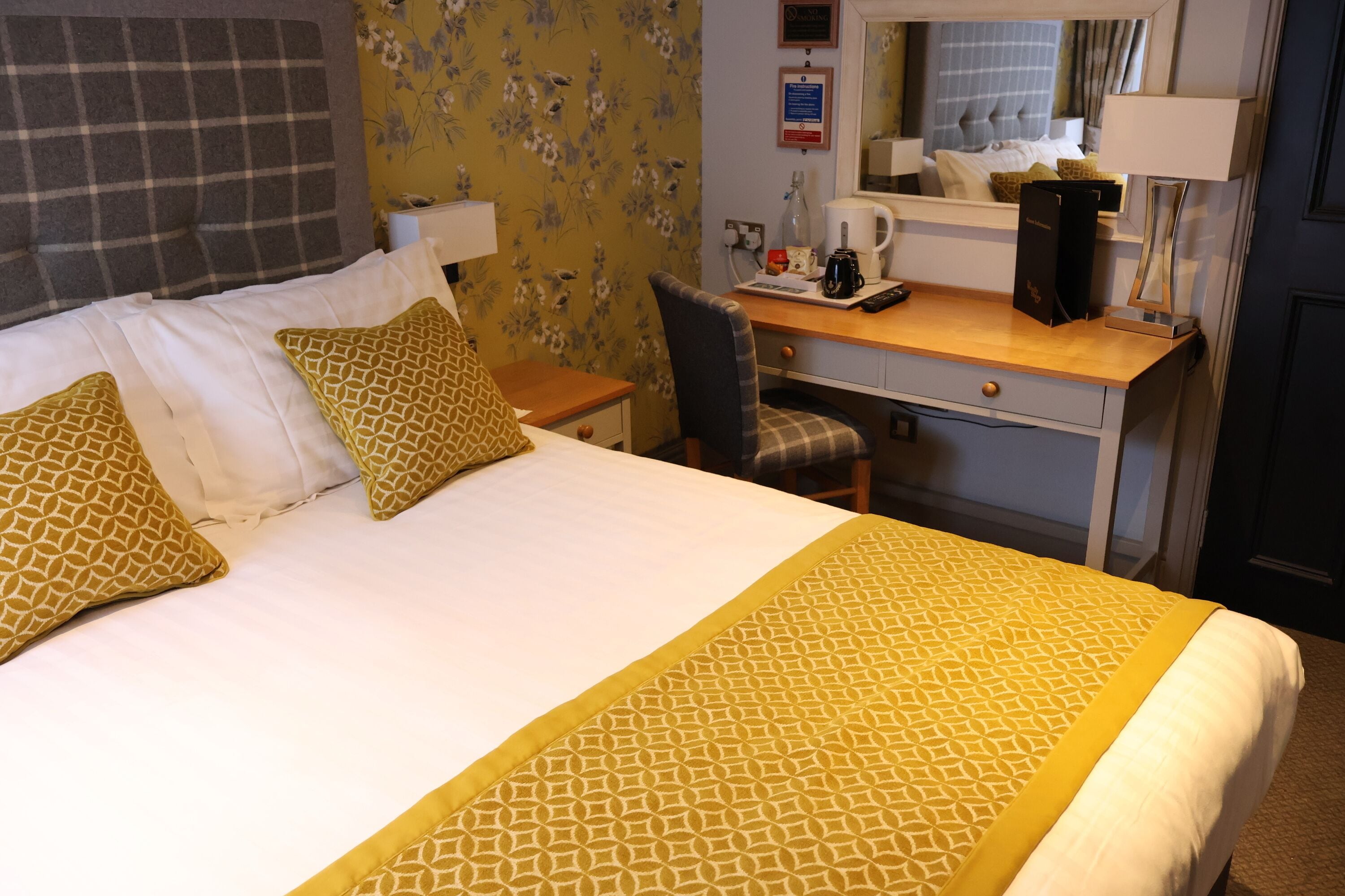Une chambre d’hôtel avec un grand lit, un bureau avec une chaise, une machine à café et un miroir.